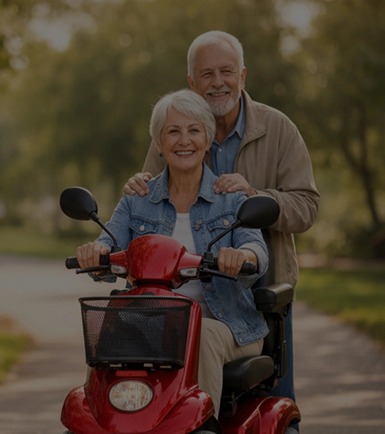 Senior couple riding a red mobility scooter in a park.