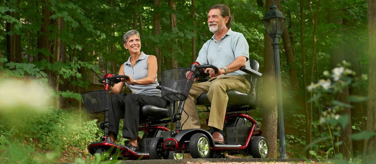 Two people using mobility scooters in a forest setting